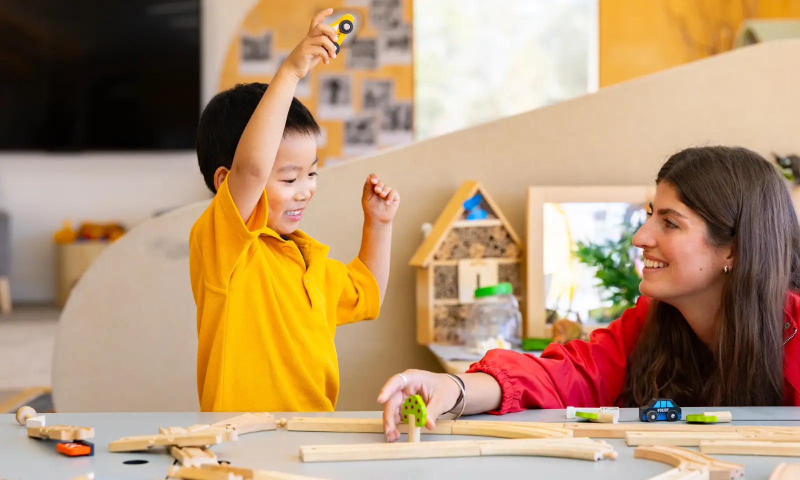 An Early Years student playing with a wooden train set with an Educational Support Assistant.
